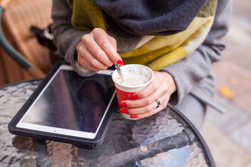 Girl stiring her coffee in the park. Tablet pc on the table. Clo