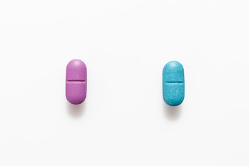 Pink pill and blue pill on white background from above