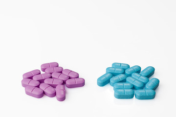 Obraz na płótnie Canvas Two heaps of pink pills and blue pills side by side on white background from above high angle
