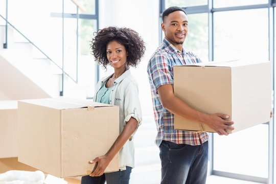 Smiling Young Couple Holding A Carton In Their New House 