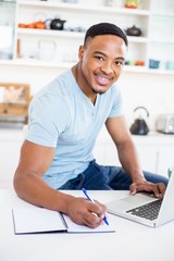 Young man using laptop while writing in diary