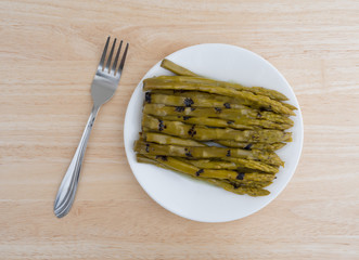 Grilled asparagus on plate with fork atop wood table