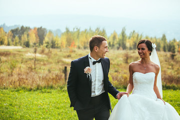 Newlywed bride and groom holding hands in autumn forest field