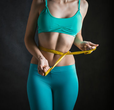 Fit and healthy young woman measuring her waist with a tape measure.