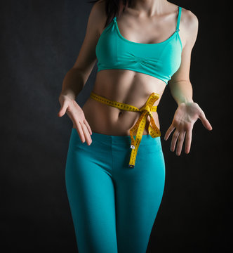 Fit and healthy young woman measuring her waist with a tape measure.