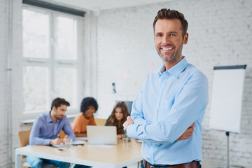 Happy businessman standing in the office with coworkers in the b