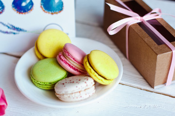 A flowers pink tulips with colorful macaroons laid on a white platter with a card and gift on a white wooden background