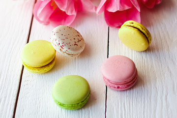A beautiful bouquet of pink tulips with colorful macaroons on white wooden background