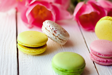 A beautiful bouquet of pink tulips with colorful macaroons on white wooden background