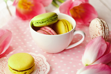 A beautiful flowers pink tulips with colorful macaroons laid in cup on white wooden background