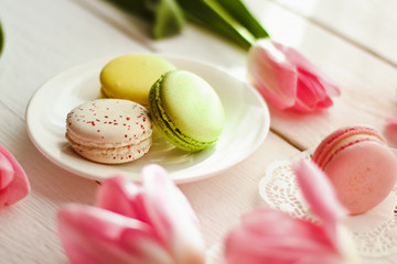 A beautiful flowers pink tulips with colorful macaroons laid on a white platter on white wooden background