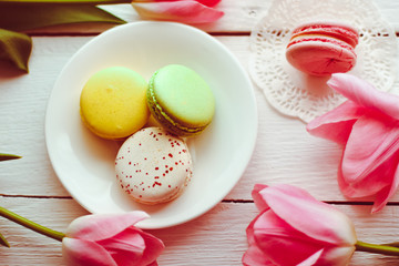 Fototapeta na wymiar A beautiful flowers pink tulips with colorful macaroons laid on a white platter on white wooden background