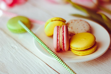 A beautiful flowers pink tulips with colorful macaroons laid on a white platter on white wooden background