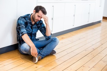 Tensed man with hand on forehead sitting on wooden floor