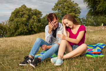 Fototapeta premium Two friends in a park with mobile phone. Summer time.