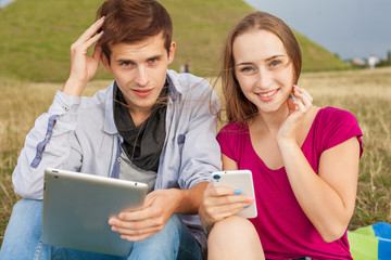 Two friends in park with mobile phone and tablet pc.