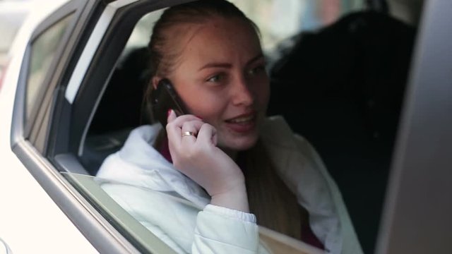 Close-up of young beautiful happy girl uses to talk smartphone sitting in the back seat of the car