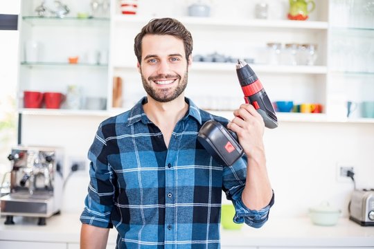 Portrait of happy man holding with drill machine in kitchen