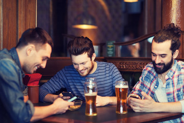 male friends with smartphones drinking beer at bar