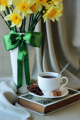 A cup of tea and a book on the background of the bouquet of daffodils..