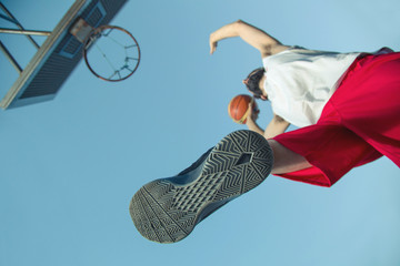 Young man jumping and making a slam dunk playing streetball, basketball from bellow. 