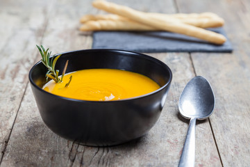 Carrot soup and pumpkin in a black bowl on a wooden table with the accompanying bread sticks on a...