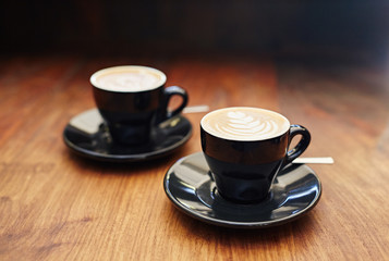 Two cappucinos in black ceramic coffee cups on wooden table