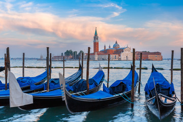 Fototapeta na wymiar Gondolas moored by Saint Mark square with San Giorgio di Maggiore church in the background in the evening, Venice, Italia