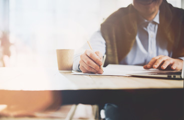 Working process. Account manager working at the wood table with new business project.Holding pencil hand, signs document and cup coffe on table. Horizontal mockup, sunny effect.Blurred, film effect
