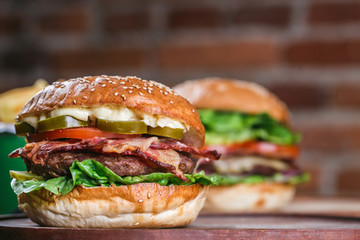 Close up on fresh burger in bun with sesame with lettuce, tomato, beef and bacon. 