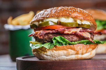Close up on fresh burger in bun with sesame with lettuce, tomato, beef and bacon. 