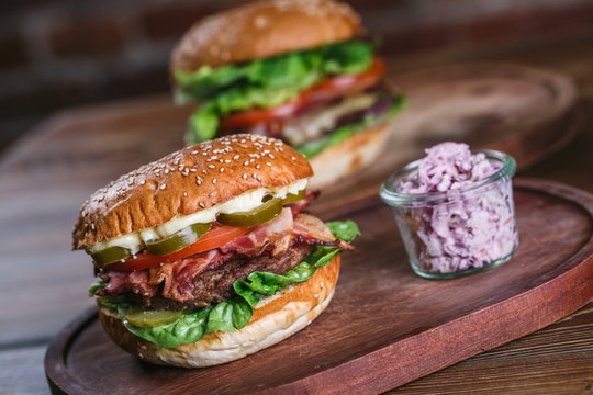 Fresh burger in bun with sesame with lettuce, tomato, beef and bacon on wooden cutting board.