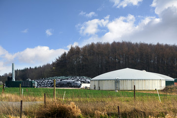Fototapeta na wymiar biogas plant for renewable energies between field and forest, blue sky with clouds