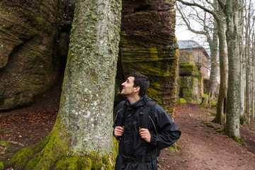Young Man,Student hiking in forest.Man hiker smiling happy portrait looking up enjoying nature on foggy day during a trekking trip. Back of a young man outdoors in nature on a hiker path in forest.