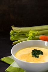 vegetable cream soup with celery and parsley garnish, dark background, vertical