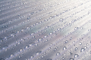 Water droplets on corrugated plastic with refracted light shinning through them at sunrise