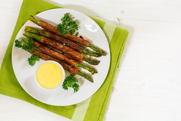 grilled green asparagus wrapped in prosciutto bacon on white wood, view from above