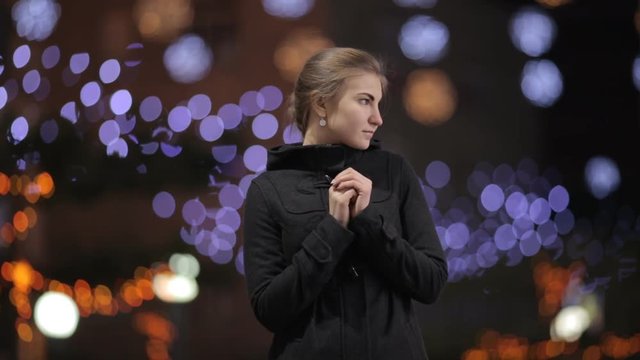 beautiful girl on the background of Christmas lights warms his hands near the face