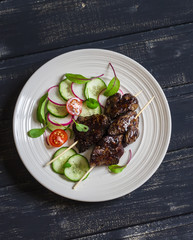 Grilled chicken liver kebabs and fresh vegetable salad on a dark wooden background