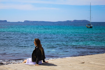 Young woman sitting on the pier with stunning view  of the sea and island