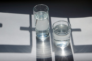 Pure water in glasses in the sunlight and in the geometric shades. Reflections and interference of light.