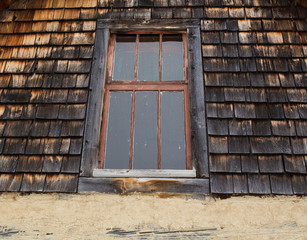 Old wood framed window in exterior top floor of decaying wood slat wall