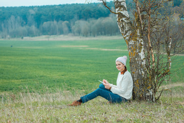 Naklejka na ściany i meble Usual pleasant hipster girl writes in a notebook. Dreamy girl on the nature