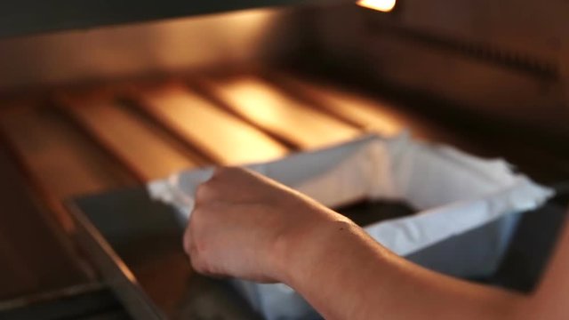 woman girl pastry chef putting trey of cake in to oven to bake