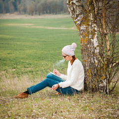 Naklejka na ściany i meble Usual pleasant hipster girl writes in a notebook and smokes. Dreamy girl on the nature