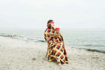 Fashion lifestyle, Beautiful young hipster woman on the beach with book and cup of tea. Relax concept. Toning.