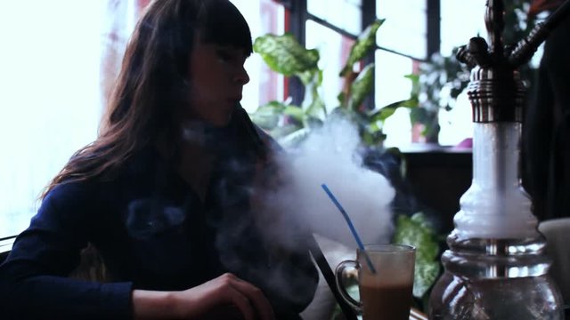 Beautiful young woman inhaling hookah. girl smoking shisha in cafe. Silhouette