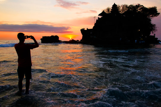 Tourist making a photo of the sunset near Tanah Lot Temple, Bali, Indonesia. 
Silhouette.