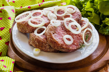 Raw cutlets on white plate on wooden background. 