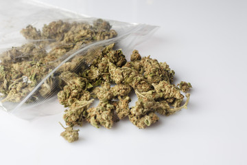 Pile of medical cannabis dried buds scattered from nylon package on white background from side